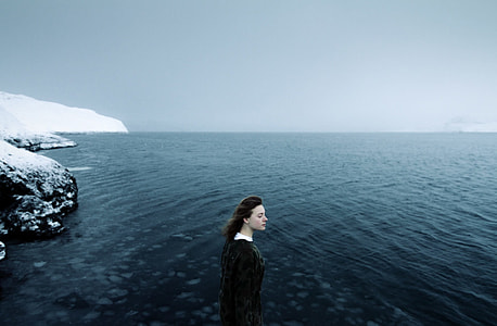 girl in black dress standing on sea shore filled with snow thumbnail