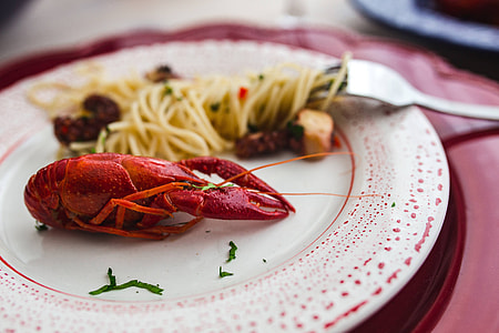 Fancy dinner with seafood pasta, crayfish and red wine by the table decorated with roses thumbnail