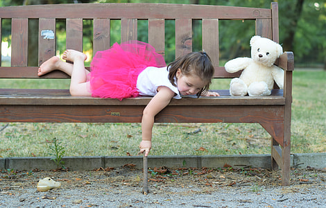 girl lying on brown wooden futon near white teddy bear holding a brown stick thumbnail