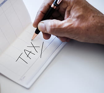 person holding ballpoint pen writing a tax word thumbnail