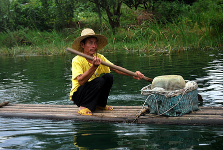 man sitting on raft while holding a bamboo stick thumbnail