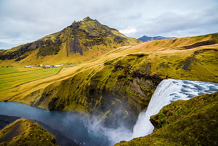 waterfalls near brown and black mountain under white and blue sky at daytime thumbnail