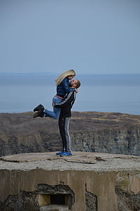 man wearing black jacket carrying woman on hilltop during daytime thumbnail