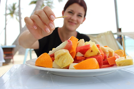woman holding toothpick about to pick variety of sliced fruits thumbnail
