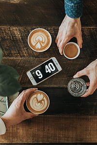 flat lay photography of person holding cup filled with brown liquids beside turned on iPhone displaying 9:40 am thumbnail