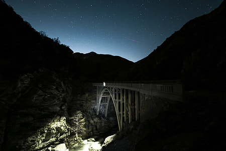 white concrete bridge over silhouette of mountain under blue sky at night thumbnail