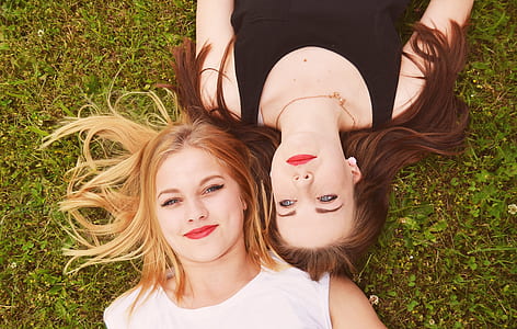 woman in black tank top lying on grass beside woman in white tank top during daytime thumbnail
