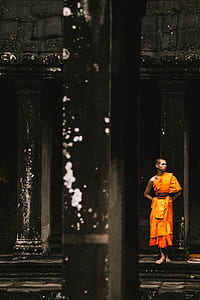 monk standing in front of black column while his hands place on his back and looking sideways thumbnail
