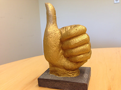 gold thumbs up ornament on brown wooden table thumbnail