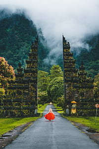 woman wearing red dress walking on spalth road in between of black concrete buildings thumbnail