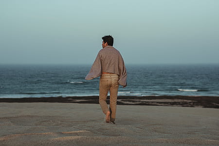 Man Walking Towards Shore With Grey Towel on Back thumbnail
