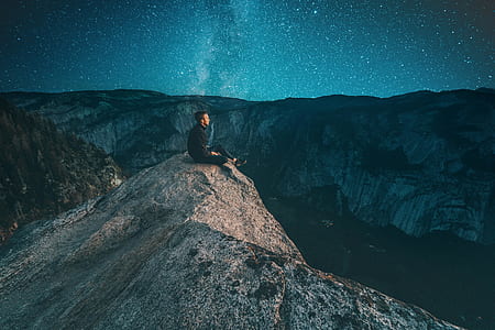 man sitting on the edge of cliff near body of water during night time thumbnail