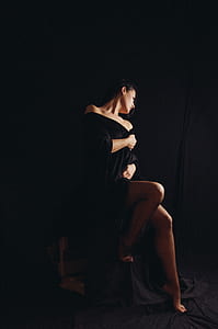 woman wearing black robe sitting in front of black covered wall thumbnail
