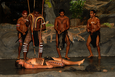 man lying on floor beside four men's holding stick thumbnail