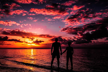 silhouette of man and woman standing on seashore during sunset thumbnail
