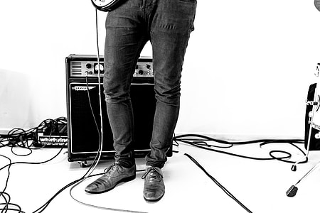 greyscale photo of person standing in front of guitar amplifier holding guitar thumbnail
