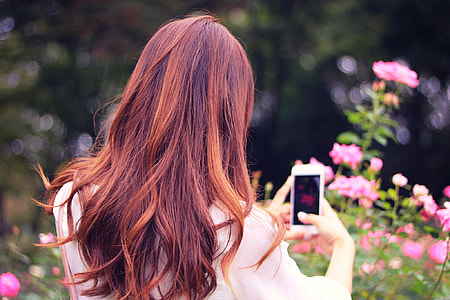 red long haired woman using her smartphone to take photo of the pink flowers thumbnail