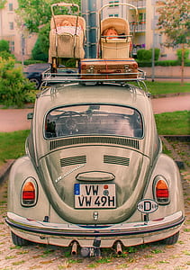 gray Volkswagen Beetle coupe with two beige doll strollers on roof rack beside brown suitcase at daytime thumbnail