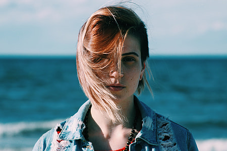 woman in distressed blue denim jacket standing near body of water thumbnail