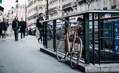 brown bike parked on black guard rail near people walking on street thumbnail