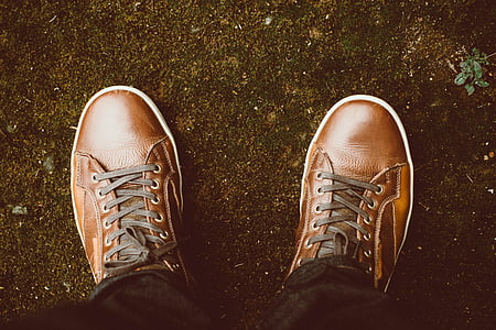 person wearing pair of brown leather lace-up sneakers standing on soil ground thumbnail