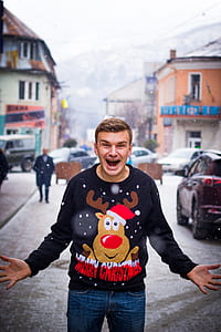 smiling man wearing black and red Merry Christmas shirt standing on street during winter season thumbnail