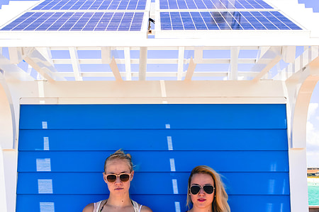 two women wearing sunglasses leaning on blue wall at daytime thumbnail