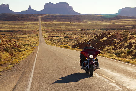 man riding on red touring motorcycle in middle of road during daytime thumbnail