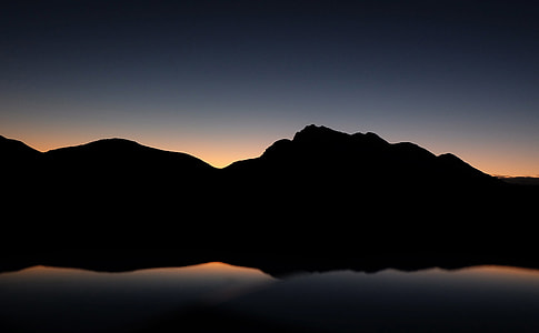 silhouette of mountain with body of water reflection thumbnail