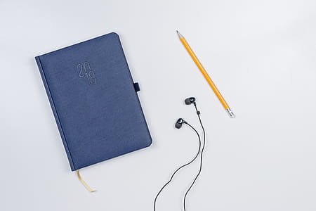 Pretty diary with a pencil and headphones on the white table. thumbnail