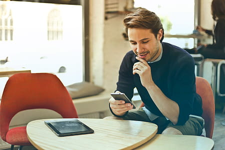 Young Man In Black Sweater Using His Smartphone While His One Hand On Chin In Restaurant thumbnail