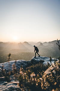 man on gray rock formation in front of green trees photo thumbnail