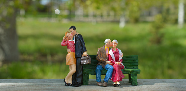 couple sitting on bench and another standing next to bench figurine thumbnail