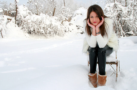 woman in white parka coat and brown snow boots sitting  on chair during snow season thumbnail