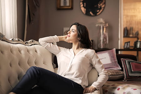 A beautiful young woman with a smile on her face relaxing on the couch looking towards the window thumbnail