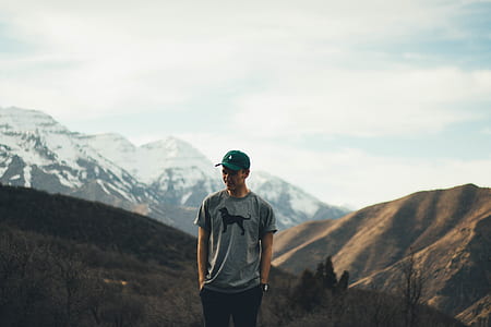 man standing with hands in pocket on mountain peak thumbnail