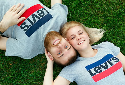 man and woman in gray Levi's crew-neck tops taking selfie while lying on green grass during daytime thumbnail