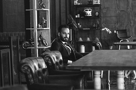 grayscale photo of a man sitting on chair in front of a table thumbnail