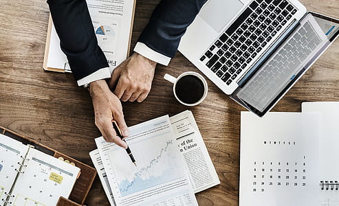flat lay photography of person writing on line graph beside cup of coffee and MacBook Pro thumbnail