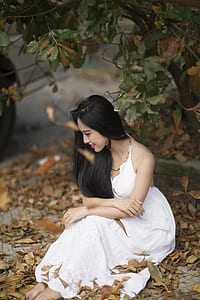 women wearing white dress sitting on brown leaves near tree thumbnail