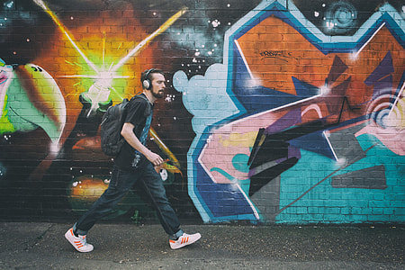 A man wearing headphones walks past vibrant street art on a wall in Shoreditch, East London. Image captured with a Canon 5D thumbnail