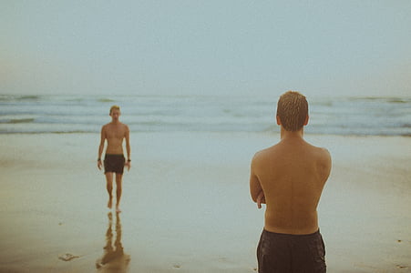 two men wears black shorts stands at seashore thumbnail