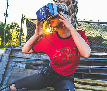Woman Wearing Red and Black Top and Blue Distressed Bottoms Wearing Gray and Black Virtual Reality Sunglasses thumbnail