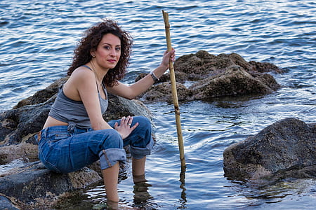 woman sitting on rock on body of water holding bamboo stick at daytime thumbnail