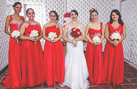 bride in white wedding dress with five women in red wedding dresses thumbnail