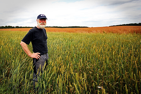 man in black crew-neck shirt wearing black cap on green and yellow corn field under white cloudy sky during day time thumbnail