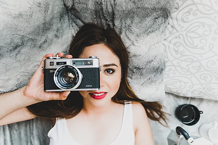 woman lying in bed white holding camera thumbnail