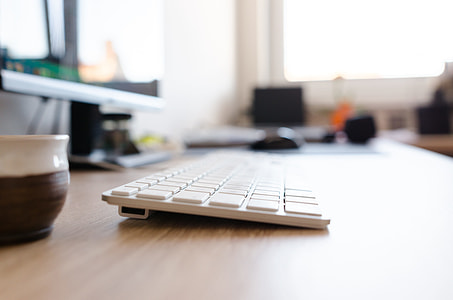 white wireless computer keyboard beside flat screen monitor on brown wooden table selective photography thumbnail