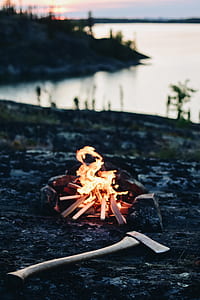 shallow focus photography of axe beside bonfire near body of water thumbnail
