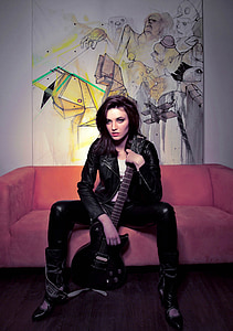 woman holding black electric guitar while sitting on the sofa thumbnail
